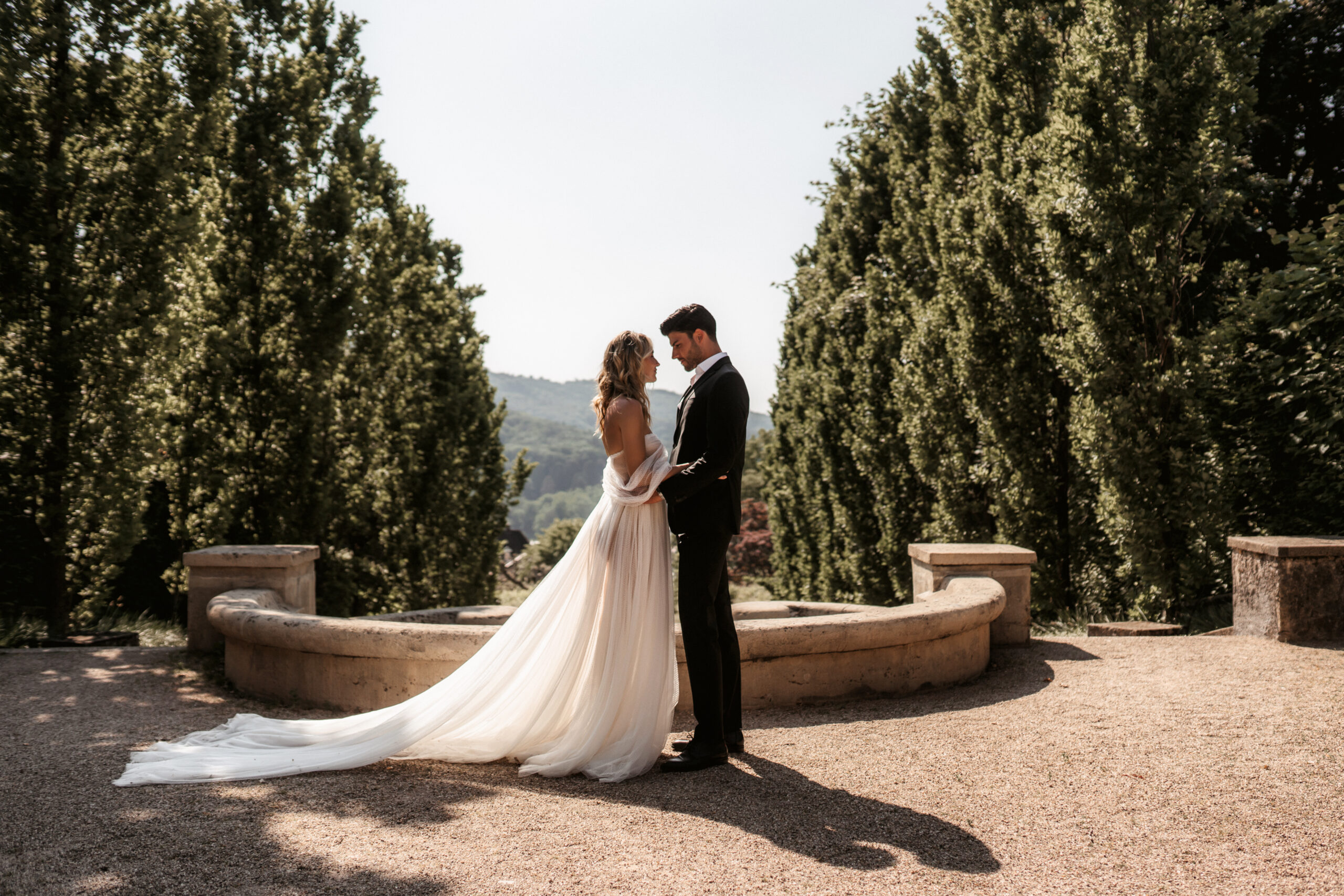 Braut und Bräutigam stehen sich auf einer sonnigen Gartenterrasse gegenüber – Hochzeitsfotografie von Kenan Egin