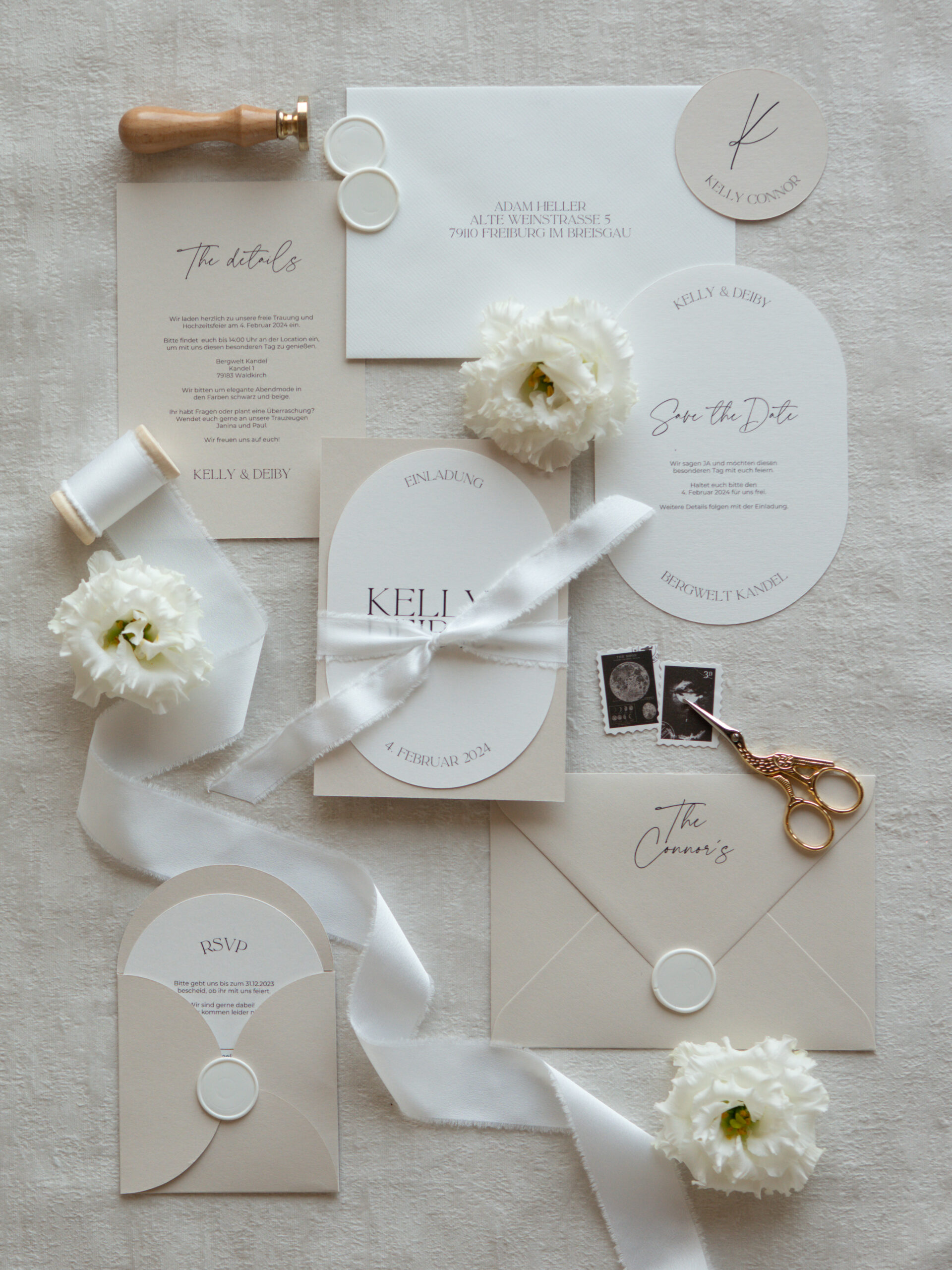 Hochzeitseinladungen in Creme und Weiß mit Seidenband, weißen Blumen und Wachssiegeln.