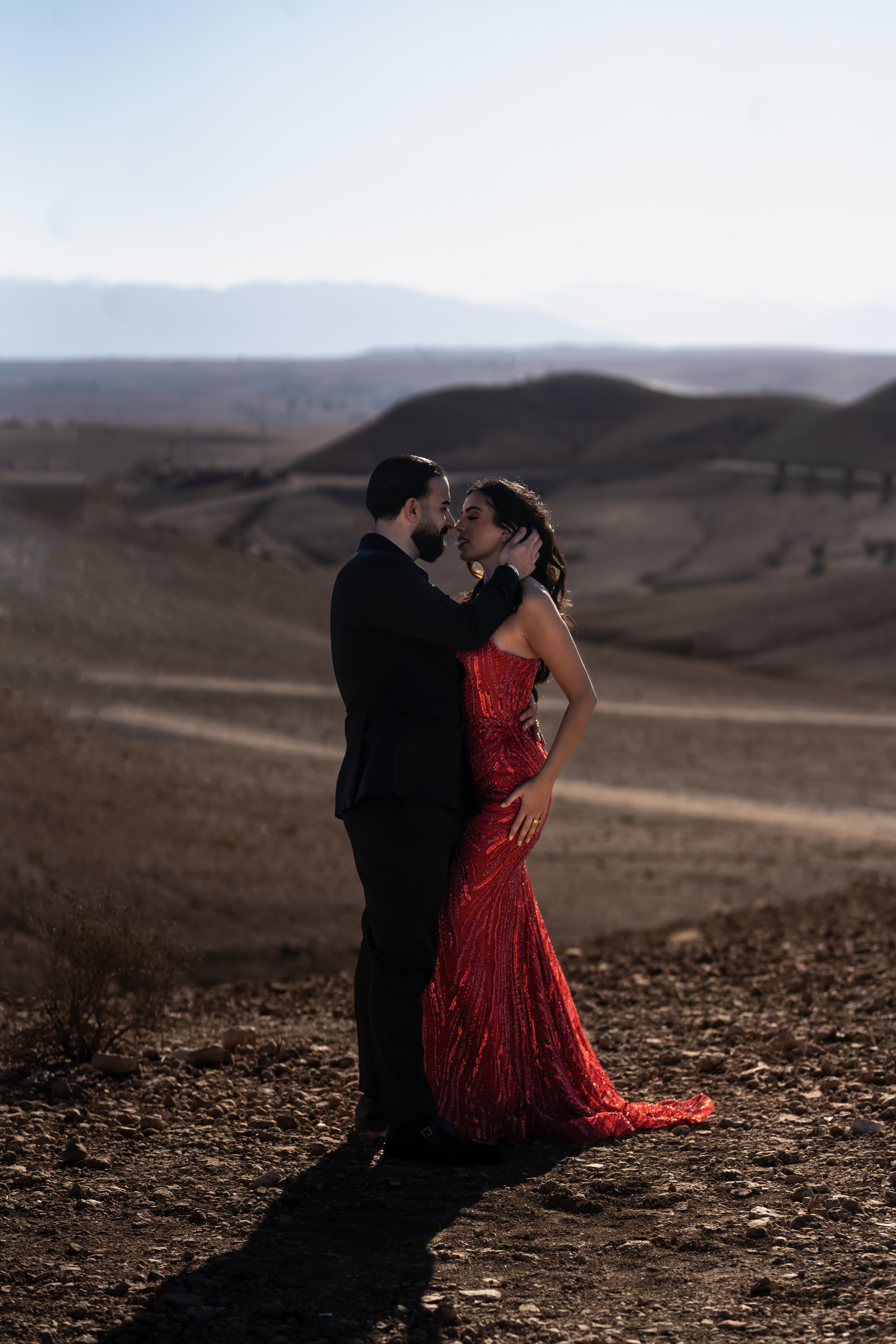 Paar in rotem Kleid und schwarzem Anzug in der Wüste bei Marakesch.