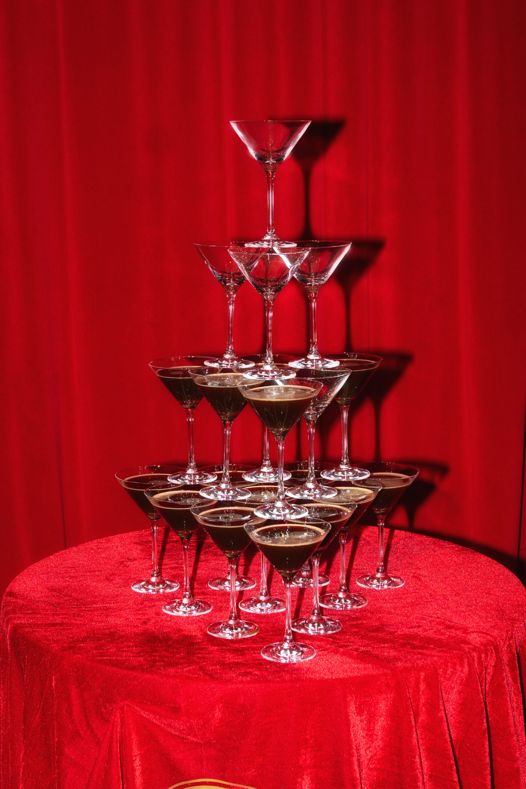Pyramide aus Cocktailgläsern auf rotem Samt vor einem roten Vorhang.